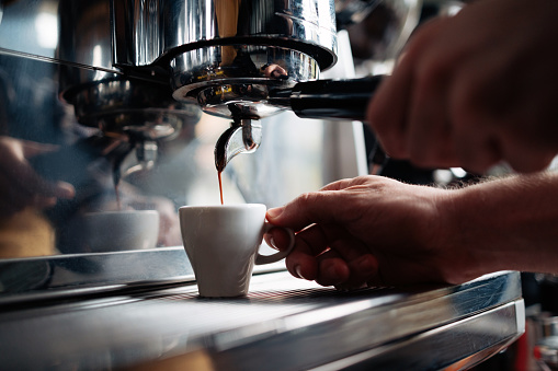 Close up photo of man hands using a coffee maker to prepare cup of coffee while standing in a retro cafeteria.