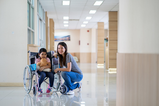 asian girl with a broken arm wearing a cast setting on wheelchair with her mother at hospital