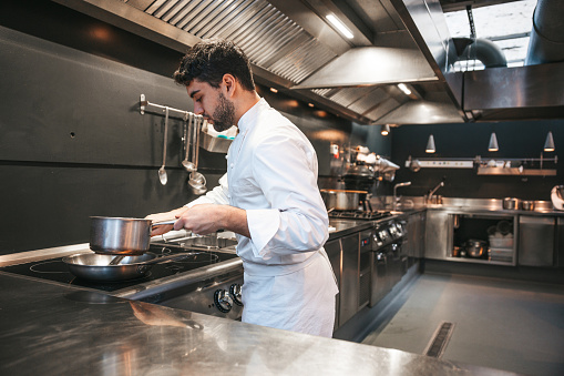 Chef preparing pasta in a luxury restaurant. Young chef cooking on glass-ceramic stove top.