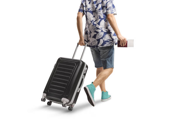 Rear view shot of a male passenger pulling a suitcase and holding a passport isolated on white background