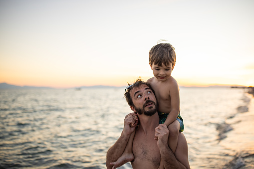 A father walking on the beach with his son sitting on his shoulders