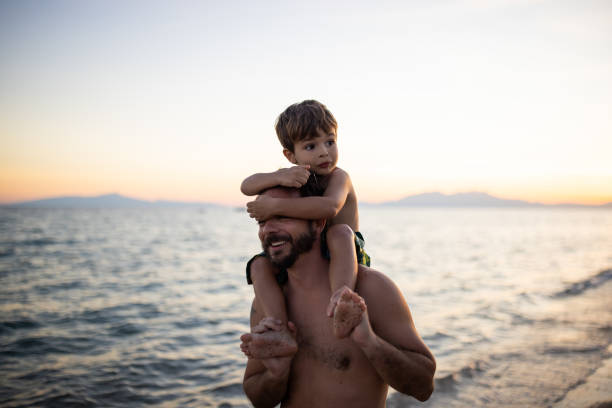 Father carrying his son on his shoulders on a public beach