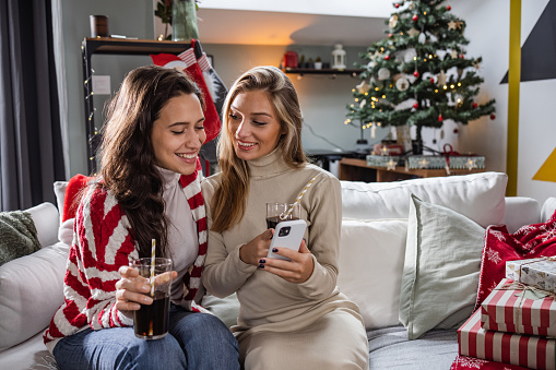 Young female friends enjoying at home. They are looking at the phone and smiling.