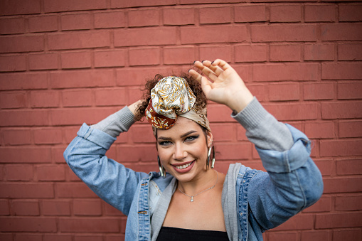 One woman, happy beautiful fashion hipster young woman, wearing a turban on her head, smiling while posing in front of a red brick wall, being cheerful, making various facial expressions