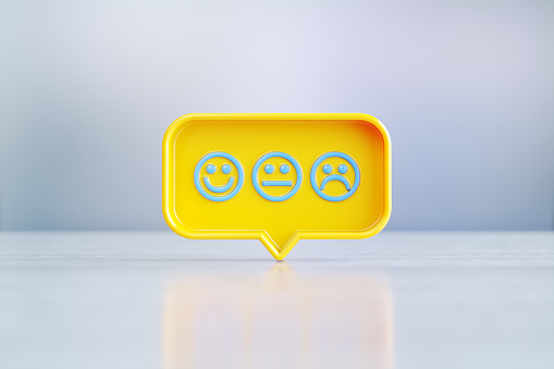 Yellow speech bubble with blue face emojis sitting on before silver defocused background. Horizontal composition with copy space.
