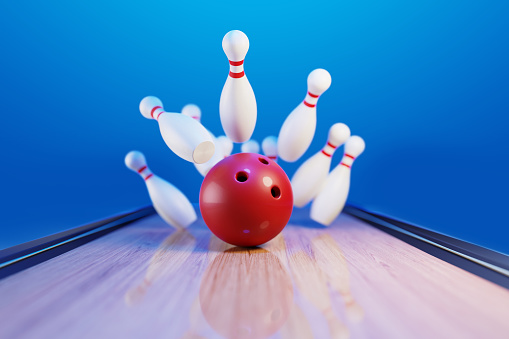 Red bowling ball hitting pins in the bowling alley before blue background. Horizontal composition with copy space. Bowling concept.