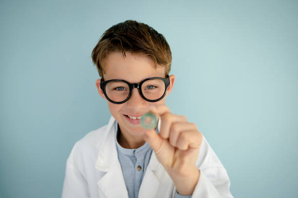 young cool boy ,with big massive black glasses is dressed up as a mad scientist holding beaker and vials in hand in front of blue background