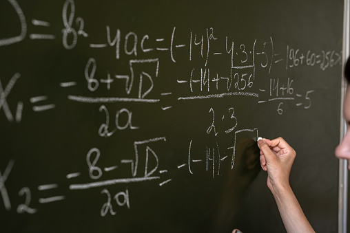 female hand writing math formulas on the classboard, close-up