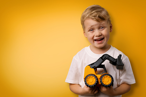 little smiling boy with toy tractor in hands on yellow background with copy space
