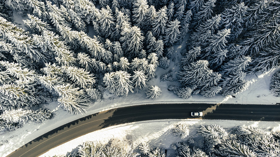 Car driving on winter mountain road. Aerial view of snowy forest with road.