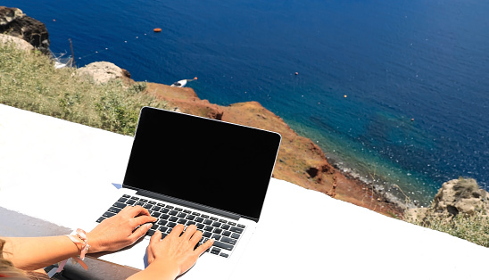 Digital nomad freelancer woman as running remotely with bright scenic view of the Mediterranean Sea ,Oia -Santorini,Greece