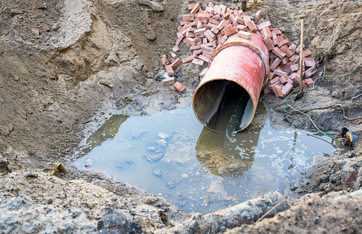 Effluent from a large open pipe spilling into the bottom of a trench during a major repair construction project.