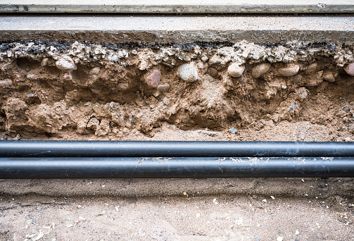 Two new modern plastic pipes installed in a large trench below the road surface.