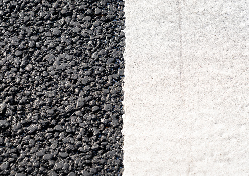 Macro image close-up of a white-line on a fresh asphalt surface, part of a zebra crossing.