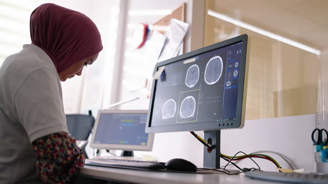 Doctor preparing a report looking at CT scan images on computer monitor in clinic