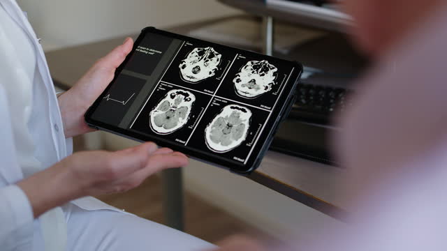 Unrecognizable doctor showing CAT scan results in digital tablet to patient