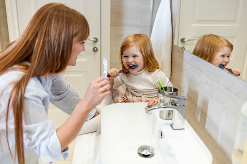 Smiling mother and daughter brushing teeth at home. Shot of a mother and her little daughter brushing their teeth in the bathroom. Shot of a beautiful young mother watching her daughter brush her teeth in the bathroom at home
