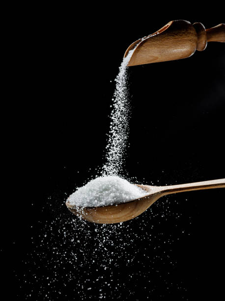 istock White refined sugar crystals falling down into the wooden spoon at black background. 1445723990