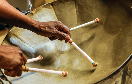 Afro American man plays the steel drum using two hands and four drumsticks