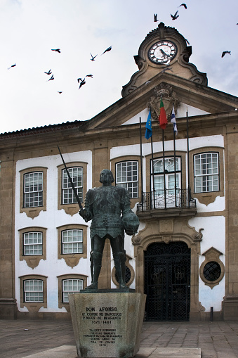 Town Hall building facade in Chaves, Portugal. Praça de Camões. Old statue of Don Afonso –  Barcelos Earl. Birds flying above.