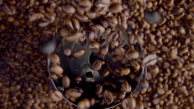 Closeup coffee seeds pouring in grinder top view. Roasted beans falling down.