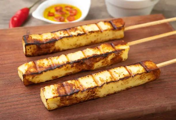 Grilled Rennet or Coalho cheese on a wooden board with sugar syrup and pepper.