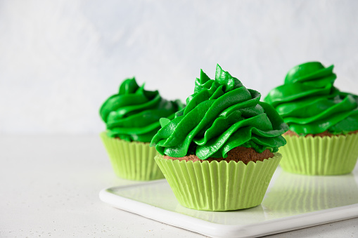 Homemade chocolate cupcake with green whipped cream and chocolate sprinkles on white background. Close up.