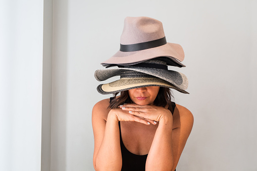 Woman wearing a pile of hats and hiding under it