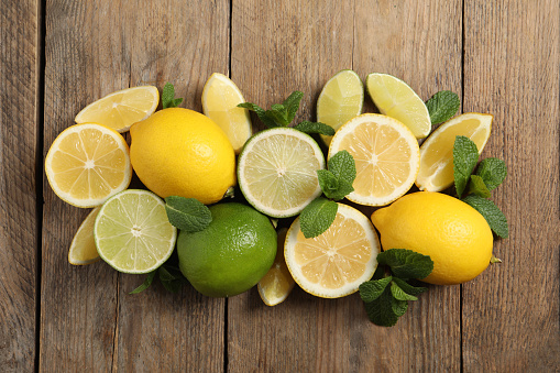Fresh ripe lemons, limes and mint leaves on wooden background, flat lay