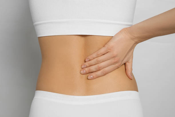 istock Woman suffering from pain in back on light grey background, closeup 1445740687
