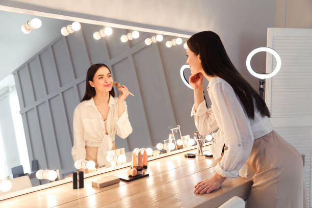 istock Young woman applying make up near illuminated mirror indoors 1445742499