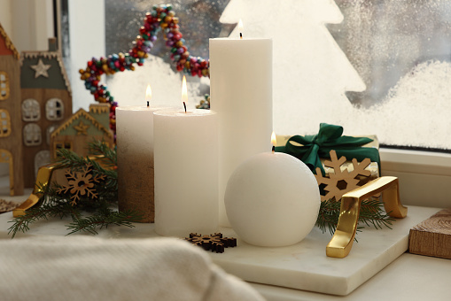 Beautiful burning candles with Christmas decor on windowsill indoors