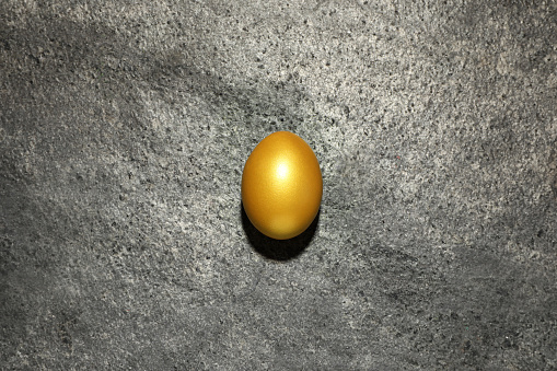 Shiny golden egg on grey table, top view