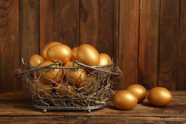木のテーブルの上の金属バスケットに光沢のある金色の卵 - shiny group of objects gem bright ストックフォトと画像