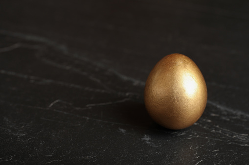 Shiny golden egg on black table, closeup. Space for text