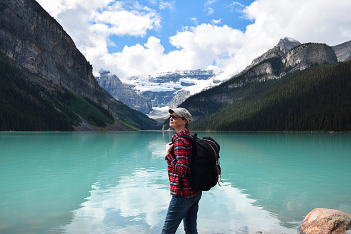 Middle aged woman with backpack standing in front of mountains and turquoise lake on her hike
