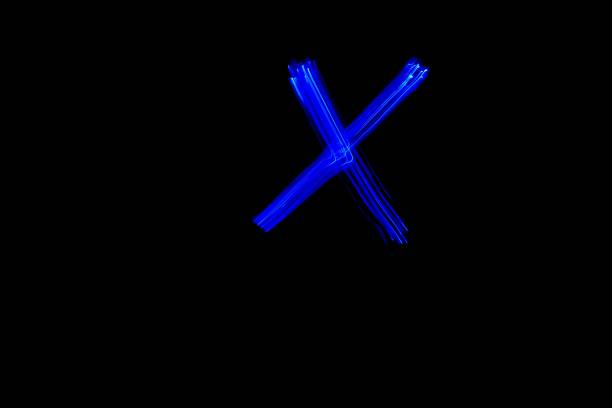 Light painting blue letter X on black background. Long exposure photo.