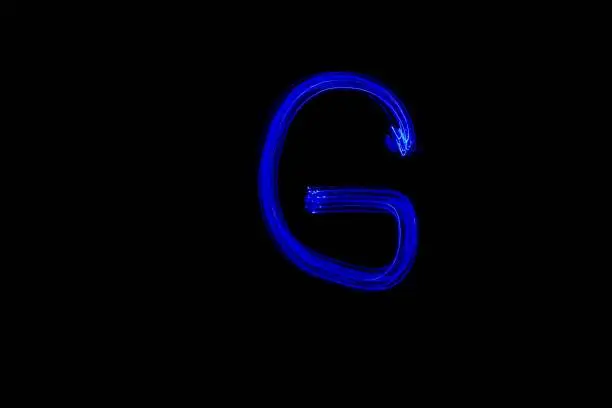 Photo of Light painting blue letter G on black background