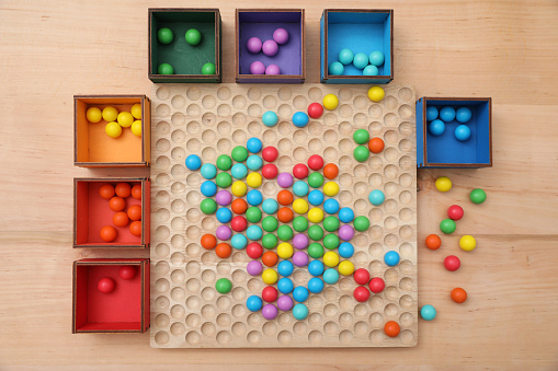 Wooden sorting board and boxes with colorful balls on table, flat lay. Montessori toy