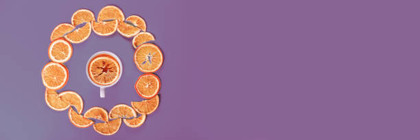 istock Circle of dried oranges with mug on violet background. Banner 1445752703