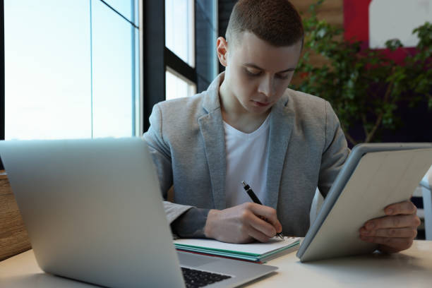 istock Young male student with laptop and tablet studying at table in cafe 1445752945