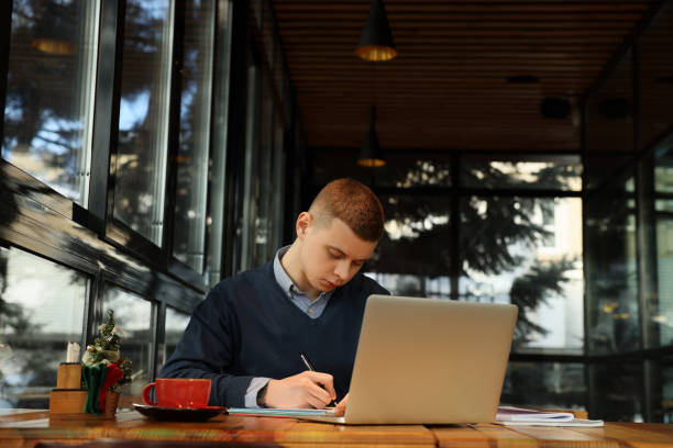 istock Young male student with laptop studying at table in cafe 1445753024