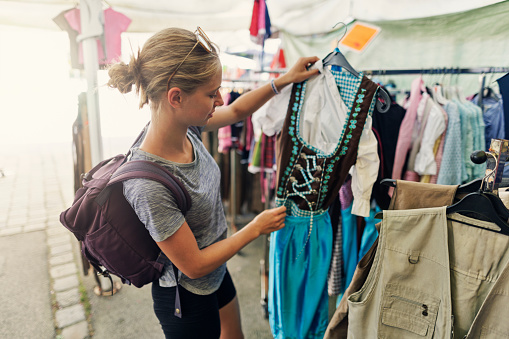 Teenage girl buying souvenirs in small Austrian town. The girl is looking at traditional dress - dirndl.\nSummer day.\nCanon R5