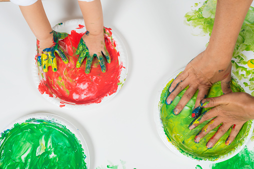 Caucasian child and teacher are playing with a plates full of finger painting color.
