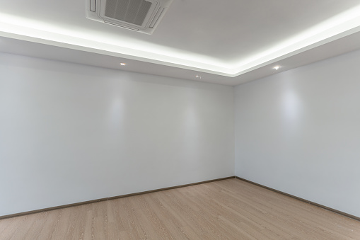 An empty white room with wooden floor and white wall and a simple white ceiling with light