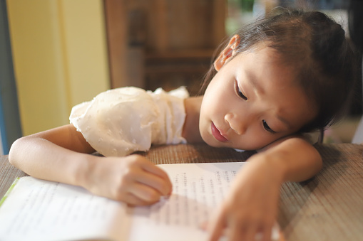 a Asian girl lying on the wooden table reading a book.