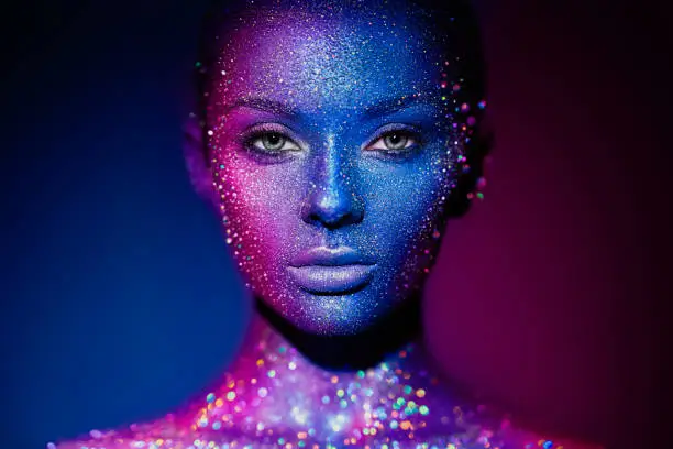 Fashion model woman in blue bright sparkles and neon lights posing in studio.  Portrait of beautiful young woman. Art design colorful glitter glowing make up