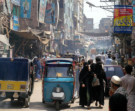 Peshawar, Khyber Pakhtunkhwa / Pakistan - Aug 15 2005: Crowds of people in a busy street in Peshawar, Pakistan. Women in burkas are shopping. It's a hot, dusty street with auto rickshaws.