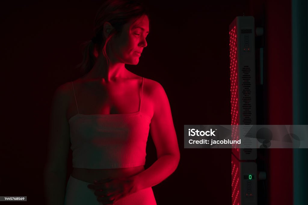 Red light therapy for beauty and skincare Mature woman receiving red light therapy. Woman standing next to a red light device in a beauty spa. Anti-aging and skin care treatment. Alternative Therapy Stock Photo