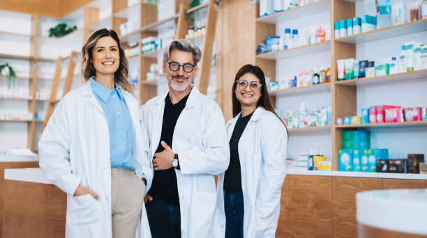 tre farmacisti in piedi insieme in un negozio di droga - healthcare and medicine smiling group of people lab coat foto e immagini stock